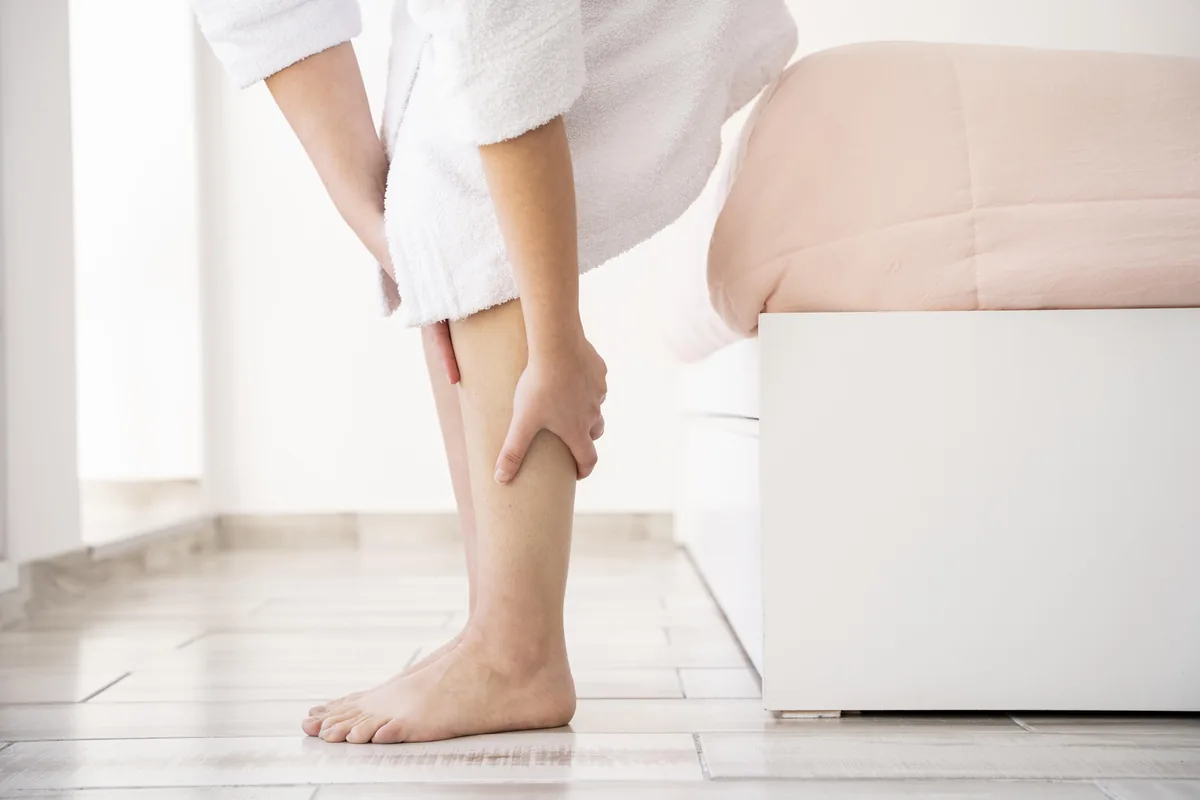 Close das mãos de uma mulher massageando a própria panturrilha