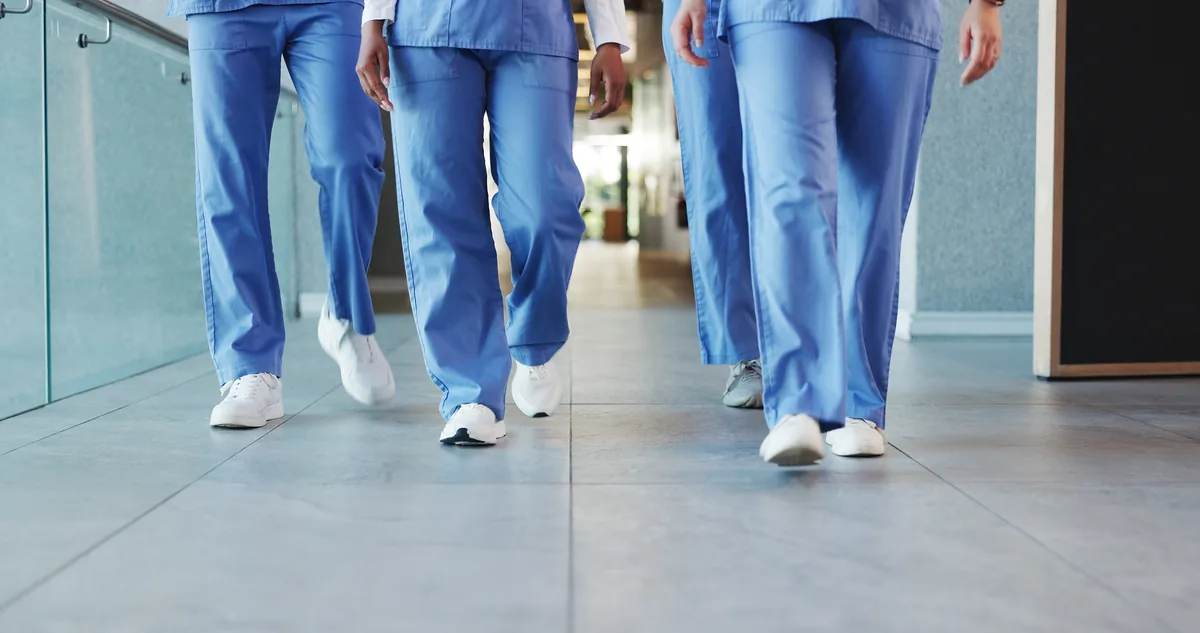 Pernas de profissionais de uniforme caminhando pelo corredor de um hospital